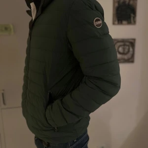 Colmar jacka - Snygg grön quiltad jacka från Colmar med dragkedja och huva. Perfekt för kyligare dagar med sin stilrena design och bekväma passform. Liten defekt på ryggen men går att sätta laglapp så märks det inte.