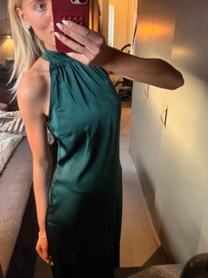Grön långklänning i satin - Snygg smaragdgrön långklänning i satin med hög hals och ärmlös design💚 Klänningen har en elegant, slät siluett och lätt glansigt material som ger en lyxig känsla. Perfekt för studentbal eller finare tillfällen! Aldrig använd, har prislapp kvar!🫶🏼