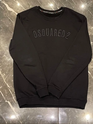 Svart sweatshirt från Dsquared2 - Stilren svart sweatshirt från Dsquared2 med broderad logga framtill. Tröjan har rund halsringning, ribbade muddar vid ärmslut och nederkant samt en relaxed passform. Perfekt för dig som gillar minimalistisk design och streetwear-vibe. Sparsamt använd och passar strl M/L