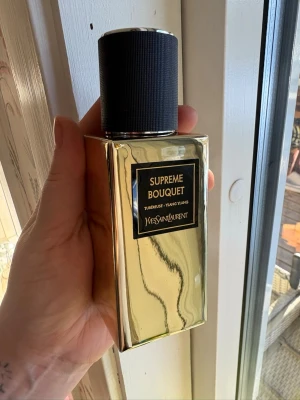 Yves Saint Laurent Supreme Bouquet parfym - Lyxig parfym från Yves Saint Laurent i doften Supreme Bouquet. Flaskan är rektangulär och har en spegelblank guldfärgad yta med svart etikett och svart kork. Märkets logga är ingraverad på korkens ovansida. Doftnoter av tuberos och ylang ylang.
