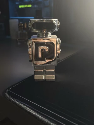 Paco Rabanne Phantom parfym robotflaska - Unik parfymflaska från Paco Rabanne i form av en futuristisk robot. Flaskan är metallisk silverfärgad med ett stort P på bröstet och har en cool, modern design som verkligen sticker ut i parfymhyllan.