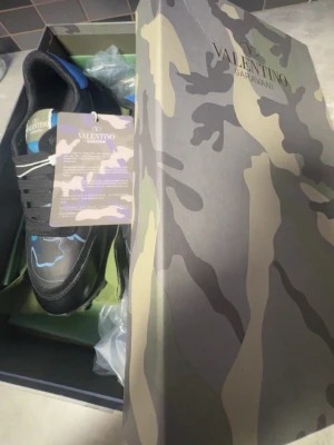 Valentino Garavani Rockrunners  sneakers - Snygga sneakers från Valentino Garavani med svart bas och blå detaljer. Skorna har ett coolt kamouflagemönster och klassisk snörning. Tillverkade i en mix av skinn och syntetmaterial för en exklusiv känsla. Perfekta för dig som vill sticka ut passar bra för vintern.