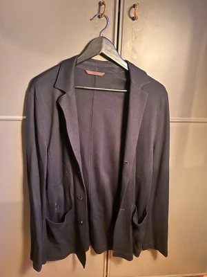 Mörkblå kavaj från Oscar Jacobson - Stilren mörkblå, tunn kavaj. Passar perfekt till skjorta eller med t shirt. Storlek S men stor i storleken. Sitter perfekt på någon som är 1.80