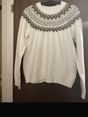 Vit stickad tröja med mönster - Säljer en vit stickad tröja med klassiskt nordiskt mönster i brunt, beige och svart runt halsen. Tröjan har rund halsringning, långa ärmar och ribbade muddar. Perfekt för kalla dagar och riktigt mysig stil.