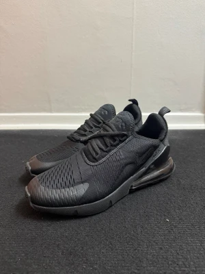 Nike Air Max 270 helsvarta sneakers - Snygga helsvarta Nike Air Max 270 sneakers med mesh-ovandel och synlig Air Max-dämpning i hälen. Skorna har en sportig siluett, diskreta loggor och en modern look. Perfekta för dig som gillar stilrena och bekväma sneakers med streetkänsla.