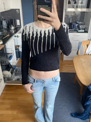 Svart och vit cropped stickad tröja - Säljer en svart och vit cropped stickad tröja med coolt grafiskt mönster.  Tröjan har långa ärmar och rund halsringning. Perfekt för dig som gillar trendiga och unika plagg. Materialet känns mjukt och skönt mot huden. Den är köpt secondhand. Jag har aldrig använt den så den inte är min stil. Den har ett tjockt och varmt tyg. Ser oanvänd ut. Frakten ingår inte i priset. 