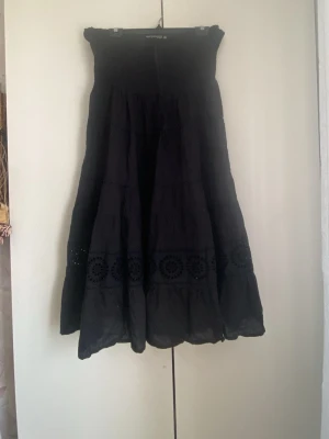 Svart långklänning med broderi - Svart långklänning med utsvängd kjol och bred smock upptill. Klänningen har dekorativa broderade detaljer i nederdelen och är tillverkad i ett lätt, luftigt tyg. Funkar också som långkjol. Som en kläning slutar den efter knäna❣️