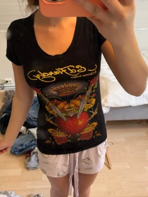 Svart Ed Hardy t-shirt med tryck - Snygg svart t-shirt från Ed Hardy med färgstarkt tryck av hjärta, rosor, kronor och texten 'In memory of true love' på framsidan. T-shirten har korta ärmar och v-ringning. Perfekt för dig som gillar statement-plagg och streetstyle.