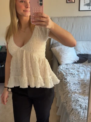 Vit spetsblus med volang från Gina  - Supersöt vit blus från Gina med v-ringning, korta ärmar och volang nertill. Blusen är i spets och har en luftig, romantisk känsla. Perfekt att styla med jeans eller kjol för en trendig look.