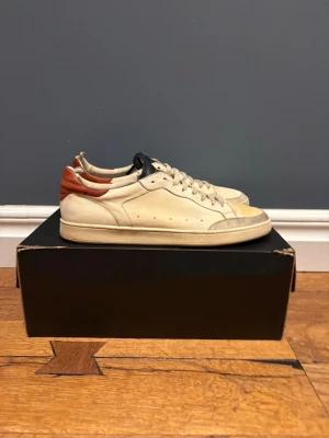 Lactea hevea sneakers - Snygga beige lactea hevea sneakers kontrasterande brun häl och mörkblå detalj på plösen. Klassisk låg profil och perforerade sidor för extra stil. Perfekta för dig som gillar minimalistisk design med en twist. Skorna kostar 6000 nya och har en sula som inte kan slitas.