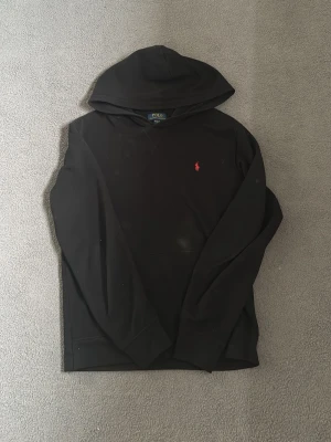 Svart Polo Ralph Lauren Hoodie - En fin polo hoodie i svart färg i storlek XL i barnstorlek vilket passar dig som är 170-175. Säljer då den ej passar mig längre och blir bara gärna av med den. Originellt köpt från Kidsbrandstore. Den har lite hårstrån men allting tas bort i tvätten, alltså ingen defekt.