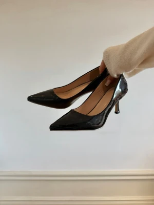 Svarta lackade klackar med spetsig tå - Snygga svarta klackar i lack med spetsig tå och smal klack. Klassisk och elegant design som ger en stilren look. Perfekta för att lyfta vilken outfit som helst. Skorna har en glansig finish och är tillverkade i syntetmaterial.