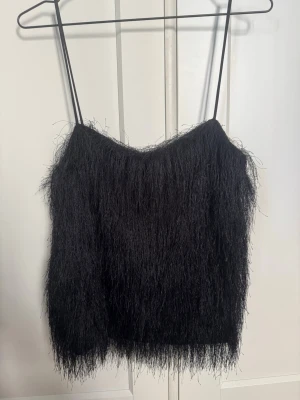 Svart fluffig linnetopp från H&M - Säljer en svart fluffig linnetopp från H&M med tunna axelband och en cool, lurvig textur. Toppen är ärmlös och har en passform som ger en trendig look. Perfekt för dig som vill sticka ut med en unik topp i garderoben.