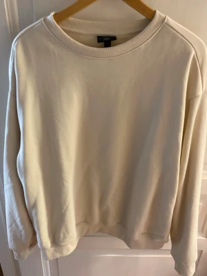 Beige loose fit sweatshirt från H&M - En stilren beige sweatshirt från H&M i loose fit-modell. Tröjan har rund halsringning, långa ärmar och ribbade muddar vid ärmslut och nederkant. Perfekt för en avslappnad och trendig look. Materialet är mjukt och bekvämt, troligtvis bomullsblandning.