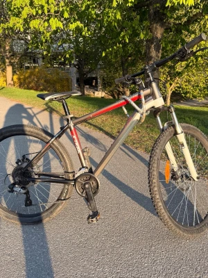 Svart och röd mountainbike - Säljer en mountainbike med svart och röd ram, grova däck och framgaffel i silver. Cykeln har flera växlar, sportig design och robust ram i metall. Perfekt för dig som gillar att cykla i terräng eller på grusvägar. Utrustad med reflexer på hjulen och bekvämt sadel.
