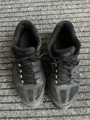 Svarta Nike sneakers med mesh och detaljer - Snygga svarta sneakers från Nike med coola paneldetaljer och meshpartier för extra andningsförmåga. Skorna har klassisk snörning och låg profil, perfekt för en sportig och urban stil. Diskret Nike-logga på plösen och sidan.