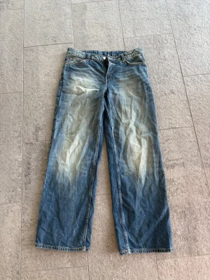 Weekday ample low loose jeans - Ett par blå jeans med rak passform. Jeansen har klassisk femficksdesign och knappgylf. Materialet är denim i bomull och färgen är ljusblå med blekta partier för en avslappnad look.