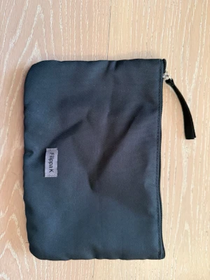 Svart necessär från Filippa K - En stilren svart necessär från Filippa K i slitstarkt tygmaterial. Väskan har en enkel rektangulär form, dragkedja upptill och en liten läderdetalj på dragkedjan. Perfekt för att organisera småsaker eller smink i väskan.