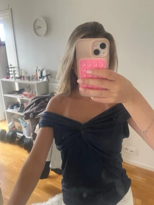 Mörkblå offshoulder topp - Snygg mörkblå offshoulder topp med twistad detalj framtill. Toppen har en croppad passform och är axelbandslös vilket ger en trendig look. Perfekt att styla med både jeans och kjol för en cool outfit.