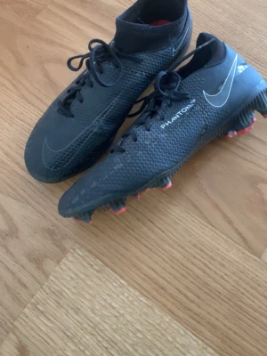 Nike Phantom Vision svarta fotbollsskor - Säljer ett par svarta Nike Phantom Vision fotbollsskor med högt skaft och snörning. Skorna har en texturerad ovandel för bättre bollkontroll och röda dobbar, vi kan snacka om priset😁