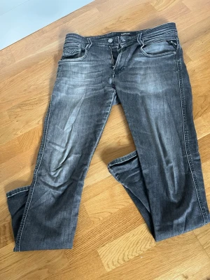 Replay svarta jeans med slitningar - Säljer ett par svarta jeans från Replay med snygga slitningar och tvättade detaljer. Klassisk femficksmodell med raka ben och vita kontrastsömmar. Perfekta för dig som gillar en avslappnad men trendig stil. 28/32