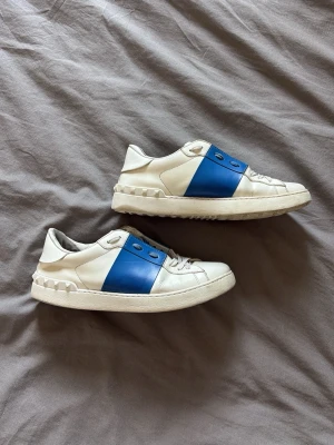 Valentino sneakers i blåvit färg - Snygga vita sneakers från Valentino med en bred blå exklusiv läder-detalj i mitten. Passar även (38/39 i strl). Skorna är faktiskt i väldigt bra skick på utsidan trots flitigt använda, insidan är sedan ett bra tag tillbaka fixad med nytt läder och funkar superbra! Bara att skicka om du har frågor🤝