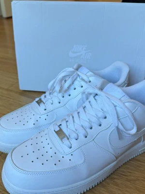 Nike Air Force 1 vita sneakers - Nästan helt nya, knappt använda! Klassiska Nike Air Force 1 sneakers i helvitt läder med perforerad tå, vita skosnören och metall-detalj vid snörningen. Swoosh-logga på sidan och broderad Nike Air-logga på hälen. Tjock sula för extra komfort och streetkänsla.