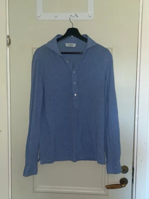 Blå långärmad henley från Gran sasso - Snygg blå henley-skjorta från Gran Sasso med lång ärm och klassisk krage. Skjortan har knappar framtill och är gjord i ett mjukt bomullstyg som känns skönt mot huden. Perfekt för en avslappnad men stilren look. Skick 6/10, lite utsliten men  fortfarande bra. Ny pris 1799 kr.