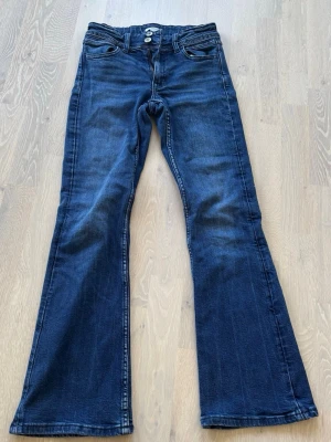 Mörkblå bootcut jeans - Snygga mörkblå bootcut jeans med klassisk femficksdesign och dubbla knappar i midjan. Jeansen har utsvängda ben och är tillverkade i denim med lätt stretch. Perfekta för dig som gillar en retroinspirerad look.