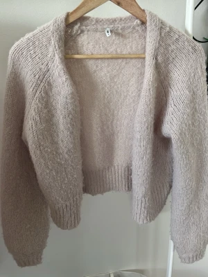Ljusbeige stickad kofta - Mysig ljusbeige stickad kofta med långärmad design och ribbade muddar. Koftan är kortare i modellen.