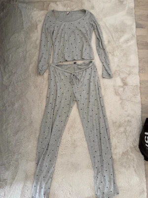 Grå pyjamas set med lång ärm - Mysig grå pyjamas set med små svarta stjärnor. Setet består av en långärmad tröja med rund hals och matchande byxor med dragsko i midjan.