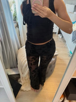 Svarta meshleggings med spetsdetaljer - Säljer ett par svarta meshleggings med snygga spetsdetaljer och blommigt mönster. De är genomskinliga och har en tight passform som framhäver benen. Perfekta för dig som vill ha en edgy och trendig look. Materialet är stretchigt och bekvämt. Helt oanvända!