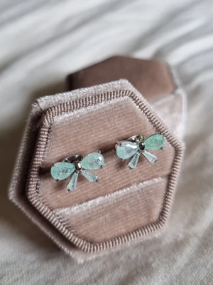 Mint Bow Earrings  - En tidlös elegans örhängen förenar en klassisk vintage-look med modern minimalism. Örhängen är prydda med ljusreflekterande kristaller i en förtrollande havsgrön nyans. .                                  Material: Rhodium , CZ-diamant Nickeltestat & allergivänligt                  Storlek: Längd ca 1,3cm Bredd ca 0.3cm -Inga prisförslag, tack.                                       - Varan packas noggrant och säkert 