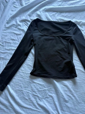 Svart långärmad topp från SHEIN - En svart långärmad topp från SHEIN i storlek Petite XXS. Toppen har en djup rundad halsringning och är figurnära med enkel design. Perfekt att matcha med jeans eller kjol för en clean look.