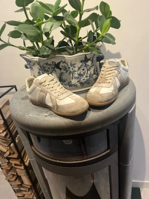 Vita masion margiela sneakers i mocka och läde - Snygga sneakers i beige mocka och vitt läder med klassisk gummisula. Modellen har lågt skaft och stilren design som passar till många outfits. Perfekta för dig som gillar en clean och tidlös look.