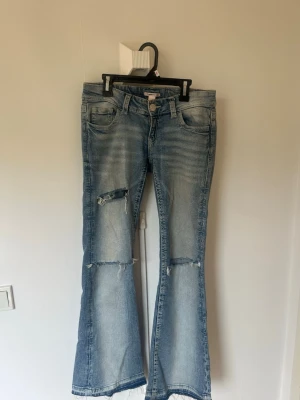 Ljusblå utsvängda jeans Gina Tricot - Säljer ett par ljusblå jeans från Gina Tricot med utsvängda ben och slitna detaljer vid knäna. Jeansen har klassisk femficksdesign, dragkedja och knapp framtill. Perfekta för en trendig och avslappnad look. Jag har sprättat upp jeansen ner till för att de ska bli längre 