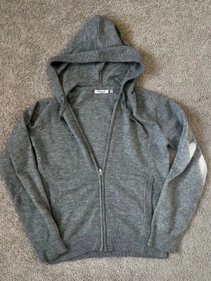 Grå hoodie med dragkedja från RYVLS - En stilren grå hoodie från RYVLS Stockholm med dragkedja framtill och två fickor. Tröjan har huva med dragsko och är tillverkad i mjukt material som känns skönt mot huden. Perfekt för en avslappnad look. Använd cirka 10 gånger inga slitningar eller hål. Jag är 168cm och den är påväg att bli för liten som ni ser på bilden 