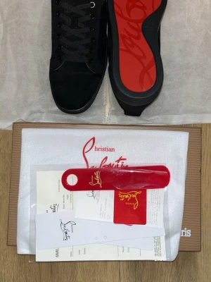Svarta sneakers från Christian Louboutin - Snygga svarta sneakers från Christian Louboutin med klassisk röd sula och diskret logga. Skorna har svarta skosnören, ovandel i mocka och detaljer i läder. Perfekta för dig som vill ha en exklusiv och stilren look med en ikonisk touch. Pris kan diskuteras.