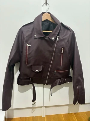 Vinröd skinnjacka - Jacka i läderimmitation, den är knappast använd och i gott skick, dock osäker på vart den är ifrån samt vilken storlek då lapparna inte finns kvar (köpt secondhand). Jag brukar ha large i jackor så skulle vilja säga att denna är S/M då den är lite för liten på mig (se bild 2) 😊