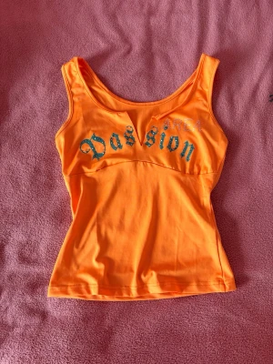 Orange linnetopp med text Passion - Snygg orange topp med tryck och glittriga detaljer framtill. Toppen har en figurnära passform och är perfekt för sommaren. Aldrig använd endast testad, storlek XS men stretchig så kan passa även S 