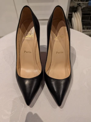Svarta pumps från Christian Louboutin - Stilrena svarta pumps från Christian Louboutin med spetsig tå och klassisk siluett. Skorna är tillverkade i slätt läder och har en elegant, tidlös design med beige innersula och diskret logga på insidan.