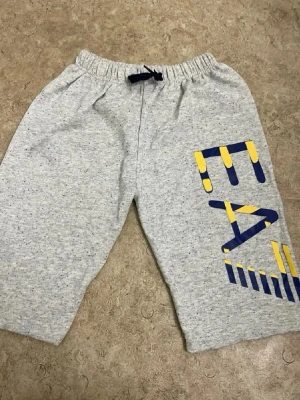 Grå mjukisshorts med tryck - Gråmelerade shorts med resårmidja och snörning. Stora grafiska bokstäver i blått och gult på ena benet ger en sportig vibe. Perfekta för chill dagar eller träning. Mjukt material för extra komfort.