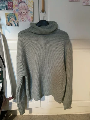 Grå/grön polotröja från H&M - Mysig grå/grön stickad polotröja från H&M med bred ribbstickning. Tröjan har en hög, vikt krage och långa ärmar med avslappnad passform. Perfekt för kyliga dagar och enkel att matcha med olika outfits. Använd några gånger men den är gott som ny. Tror den var 299kr men jag har ej kvar prislappen. Säljer för 150kr. Storlek L men jag tycker den är lite oversized