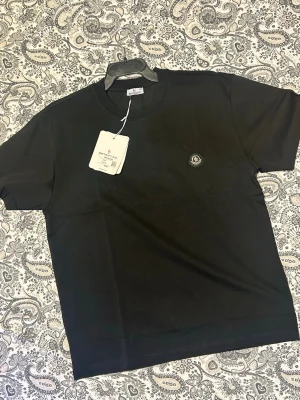Svart t-shirt från Moncler, helt ny  - Snygg svart t-shirt från Moncler med klassisk passform och rund hals. T-shirten har korta ärmar och en liten Moncler-logga på bröstet. Tillverkad i mjuk bomull som känns skön mot huden. Perfekt till jeans eller shorts.