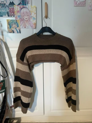 Brun cropped stickad tröja Shein - Säljer en brun, beige och svart cropped stickad tröja från Shein. Tröjan har breda ränder, rund halsringning och långa ärmar. Perfekt för lager på lager och en trendig look. Köpt för 179kr säljer för 90kr. Knappt använd, utan defekter.