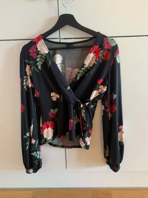 Svart blommig omlottopp med knyt - Fin blus som går omlott framtill. Väldigt mjukt och skönt material.