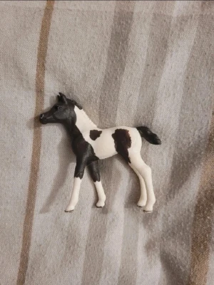 Svartvit hästfigur i plast - Säljer en liten hästfigur i plast med svart och vit färg. Figuren har tydliga detaljer som man, svans och ben, och är perfekt som dekoration eller leksak. Passar dig som gillar djur eller samlar på figurer.