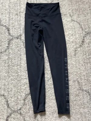 Svarta tights från Röhnisch XS - Svarta tights från Röhnisch med hög midja och diskret logga längs benet. Tillverkade i stretchigt funktionsmaterial som ger bra rörelsefrihet och sitter skönt vid träning. Snygg och enkel design som passar till alla sportaktiviteter.