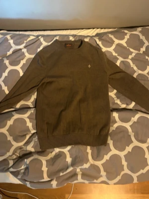 Beige stickad tröja Morris - Snygg Beige stickad tröja från Morris med rund halsringning och diskret broderad logga på bröstet. Tröjan har långa ärmar och ribbade muddar vid ärmslut och nederkant. Perfekt för lager på lager och stilrena outfits.