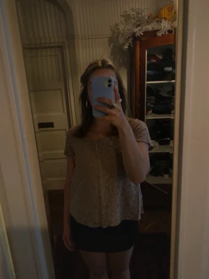 Grå/beige spetsblus med rund hals - Söt grå / beige blus med korta ärmar och rund halsringning. Blusen är täckt av spets och har en lätt a-linjeformad passning. Perfekt för dig som gillar romantiska detaljer och vill ha en luftig topp till sommaren.